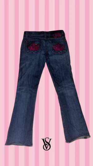 Rock & Republic blå bootcut jeans - Snygga blå jeans från Rock & Republic med bootcut passform. Jeansen har rosa detaljer, inklusive sömmar och knappar, samt broderade kronor i rosa på bakfickorna. De har nästan inga synliga defekter men det har försvunnit lite rosa färg på knapparna så de silvriga lyser igenom (visar på bild 5) men det syns inte så tydligt. 