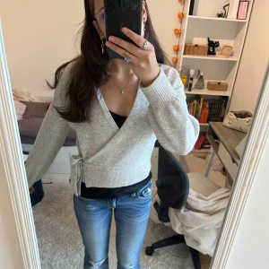 Grå omlottkofta från & Other Stories - Superfin ljusgrå omlottkofta från & Other Stories i mjukt stickat material. Koftan har knyt i sidan, v-ringning och långa ärmar. Perfekt till jeans eller kjol för en chill och snygg look.