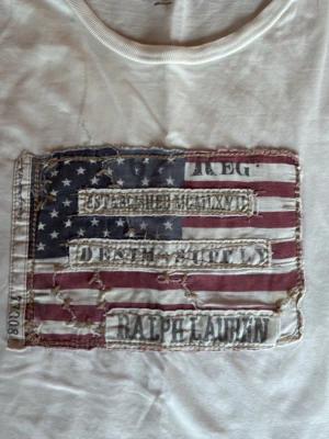 Vit t-shirt Ralph Lauren Denim & Supply -  vit t-shirt från Ralph Lauren Denim & Supply i storlek M. T-shirten har ett stort tryck med Ralph Lauren text o broderade detaljer på bröstet. Rund hals och korta ärmar. Materialet är 100% bomull