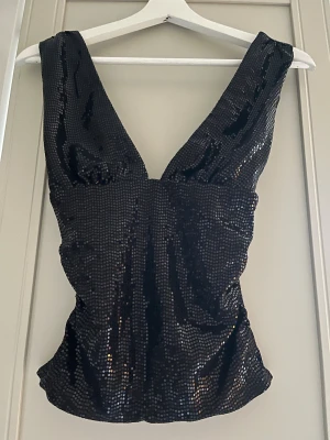 Svart glittrig topp från Bershka storlek S - Säljer en svart glittrig topp från Bershka med djup v-ringning och breda axelband. Toppen har ett snyggt paljettmönster som ger extra shine och är figurnära i modellen. Perfekta nyårstoppen!! Storlek S, helt ny och oanvänd med prislapp kvar. 