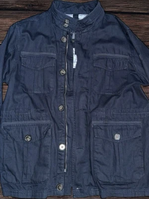 Mörkblå parkajacka från Fynch-Hatton - Parkajacka i mörkblå bomull från Fynch-Hatton med ståkrage, flera fickor med lock och knappar, samt dragkedja och knappstängning framtill. Insidan har ett ljust blommigt mönster. Perfekt för dig som gillar funktionella detaljer och stilren look.