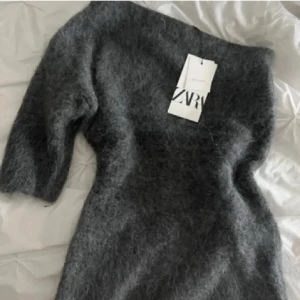 Mörkgrå oneshoulder topp från Zara - Säljer en fluffig och mjuk mörkgrå oneshoulder topp från Zara. Toppen har en asymmetrisk design med en ärm och är tillverkad i en lyxig alpackablandning. Perfekt för dig som gillar unika och trendiga plagg med cozy vibe.