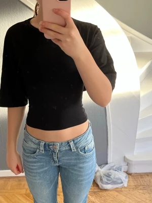 Svart croppad topp med knyt i ryggen - Svart croppad topp från lager 157 med rund hals och halvlånga ärmar. Toppen har öppen rygg med snygg knytning bak som ger en cool detalj. Tillverkad i mjuk bomull som känns skön mot huden. Perfekt att styla med jeans eller kjol för en trendig look.