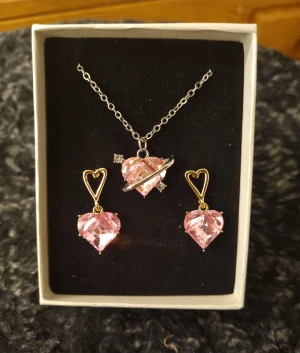 Smyckesset (A)  - Smyckeset med ett justerbart halsband i silverfärg och örhängen i guldfärgade detaljer. Material : koppar och zirkonia 