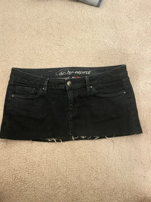  jeanskjol från edc by Esprit - svart/mörkgrön jeanskjol från edc by Esprit med klassisk femficksdesign, knapp och dragkedja framtill samt rå kant nedtill för en edgy vibe. Baktill finns två fickor med broderad detalj och en läderpatch med logga. Perfekt för dig som gillar streetstyle.