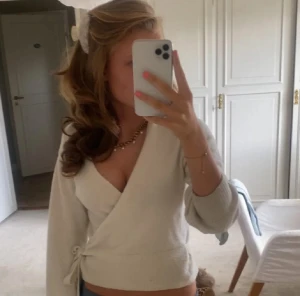 &otherstories kofta 💗💗 - Säljer en beige/vit omlottopp med knyt i sidan och djup v-ringning. Toppen har långa ärmar och är tillverkad i ett mjukt stickat material som känns skönt mot huden. Perfekt för dig som gillar en feminin och trendig look.