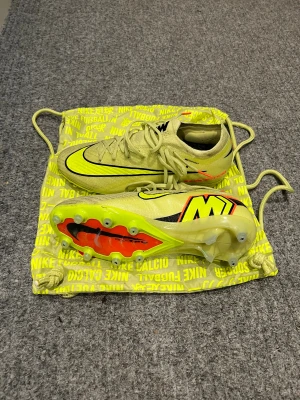 Nike mercurial elite ag max voltage - Säljer ett par Nike Mercurial Agfotbollsskor i en riktigt fräsch gul färg med svarta och röda detaljer. Skorna är köpta på Unisport och endast använda ett träningspass. Skorna har snörning och en platt sula med dobbar för bästa grepp på planen. Ny pris 3100kr