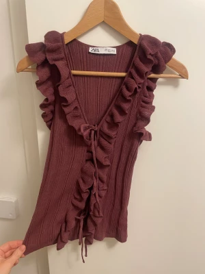 Vinröd topp  - Supersöt vinröd linnetopp från Zara med volangkant längs axlar och framstycke. Toppen är ribbad och har knyt framtill för extra detalj. Ärmlös och i mjukt stickat material som känns skönt mot huden. Endast använd en gång🥰