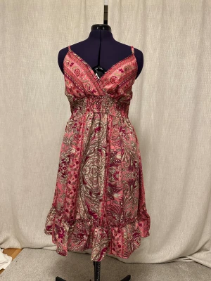 Rosa paisleymönstrad klänning från Boho - Supersöt rosa och vinröd klänning från Boho med paisley- och blommönster. Klänningen har smala axelband, omlott-v-ringning, smock i midjan och volangkant nertill. Perfekt för dig som gillar boho-stil och vill sticka ut med färg och mönster.
