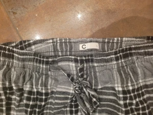 Gråsvarta rutiga mjukisbyxor med snörning - Rutiga mjukisbyxor i grått och svart med vit detalj, elastisk midja och snörning framtill. Perfekta för chill dagar hemma eller när du vill vara extra bekväm. Mjukt material och avslappnad passform.