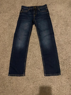 Baggy Jeans, 158 - Mörkblå jeans med snygg blekning vid knäna. Passformen är baggy och har en fem fickors design, jeansen är aldrig använda och har storleken 158.