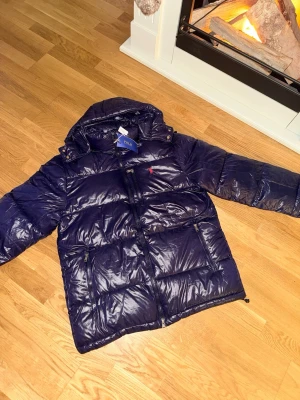 Ralph lauren jacka - Säljer nu denna helt nya glänsiga och mörkblåa Ralph Lauren-jackan i strl S. Perfekt nu när vintern är här. Som sagt helt ny och aldrig använd. Bara att skriva ett meddelande vid intresse!