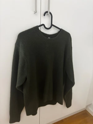 Mörkgrön stickad tröja från uniqlo - En enkel och snygg mörkgrön stickad tröja från uniqlo med rund hals och långa ärmar. Tröjan har en loose passform och är perfekt för att hålla dig varm under kyliga dagar. Materialet är mjukt och skönt mot huden.