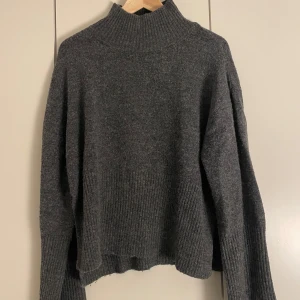 Mörkgrå stickad tröja från Gina Tricot - Mysig mörkgrå stickad tröja från Gina Tricot i. Tröjan har ribbad polokrage, långa raka ärmar och ribbade muddar. Snygg slits i sidorna och loose fit som ger en chill vibe. Perfekt för kalla dagar och enkel att styla med jeans eller kjol.