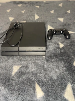 PlayStation 4 - Sony PlayStation 4 spelkonsol i gott skick med tillhörande strömkabel och en original DualShock 4-kontroll. Konsolen visar minimalt slitage och fungerar utmärkt för gaming och underhållning. Perfekt för både nya och erfarna spelare.