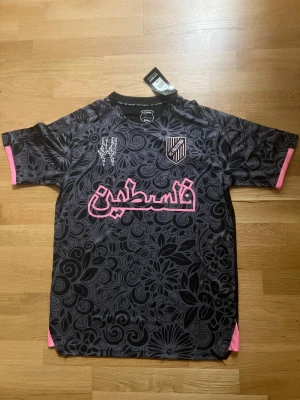 Palestina Fotbollsströja - Palestina fotbollströja i svart/grått/rosa-färger. Helt ny och oanvänd i storlek M 🙂