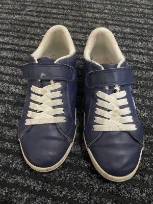 Sneakers - Marinblå och vita sneakers från H&M, med vita snören och kardborreband och blå och vita ränder på sidan. De är unisex, i storlek 33 och inte jättemycket använda.