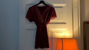 Vinröd spetsblus från Aya Moda - Supersnygg vinröd blus med v-ringning och korta ärmar i spets från Aya Moda. Blusen har omlottkänsla, knyt i midjan och vackra spetsdetaljer över axlar och ärmar. Perfekt för dig som gillar romantisk stil och vill sticka ut med färg.