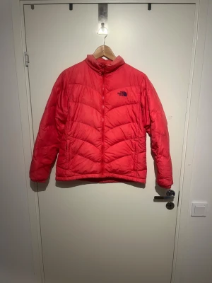  The North Face - Säljer en röd dunjacka från The North Face med broderad logga på bröstet och “600” på ärmen. Jackan har dragkedja framtill, två sidofickor med dragkedja och elastiska muddar. Perfekt för kalla dagar och har en schysst, puffig look.  Pris kan diskuteras. Skicks gärna, bud. 