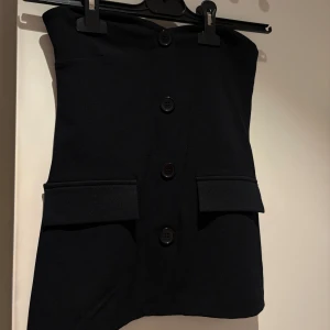Svart tubtopp med knappar och fickor - Säljer min absolut favorit topp från Gina. Det är en en bandue med knappar plus fickor. Säljes då den tyvärr blivit för liten.