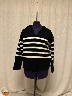 Svartvit randig stickad tröja Zara - Svart och vit stickad tröja från Zara med breda horisontella ränder. Tröjan har en djup v-ringning, stor krage och långa ärmar. Materialet är mjukt och ribbat vid kragen och muddar. Perfekt för dig som gillar en chill och stilren look.