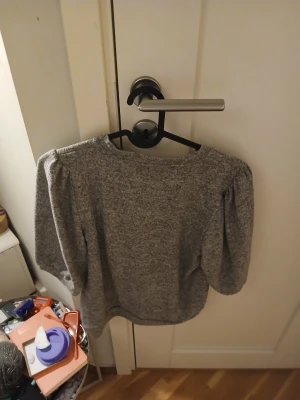 Grå stickad tröja med puffärm - Mysig grå stickad tröja med rund hals och puffiga ärmar. Tröjan har en enkel, stilren design och är perfekt för dig som gillar en chill och trendig look. Materialet är mjukt och ger en skön känsla mot huden. Passar dig som vill ha något bekvämt och snyggt.