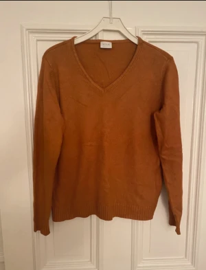 Brun stickad V-ringad tröja från Vila - Snygg brun stickad tröja från Vila i storlek XL. Tröjan har en klassisk V-ringning, långa ärmar och ribbade muddar vid ärmslut och nederkant. Perfekt för dig som gillar enkel och stilren design med en varm färgton.
