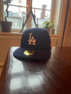 Blå LA Dodgers 59FIFTY keps New Era - Säljer en klassisk blå LA Dodgers 59FIFTY keps från New Era. Kepsen har broderad LA-logga framtill, MLB-logga bak och New Era-logga på sidan. Tillverkad i 100% polyester och har en rak skärm. Perfekt för dig som vill ha en clean och sportig look. Storlek 7 (55.8cm)
