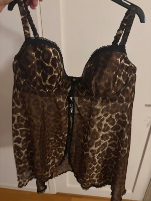 Leopardmönstrad transparent väst - Snygg väst i transparent material med leopardmönster i bruna och svarta toner. Västen har vadderade kupor, justerbara axelband och spetsdetaljer längs kanterna samt en liten blomdetalj framtill. C kupa