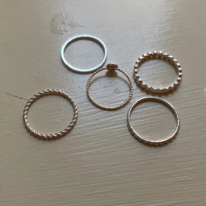 Fem tunna silverringar i olika mönster - Säljer ett set med fem tunna silverfärgade ringar i olika mönster – tvinnad, slät, pärlad och med små detaljer. Perfekta att mixa och matcha för en personlig stil. Passar både som stackable rings eller var för sig.