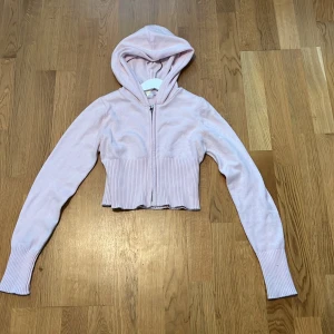 Ljusrosa croppad kofta från Gina Tricot - Superfin ljusrosa croppad kofta från Gina Tricot med dragkedja framtill och ribbade muddar. Tröjan har huva och är långärmad. Har används ungefär 1 gång, säljer då den har blivit förliten.