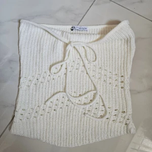 Vit stickad tubtopp från Zara - Säljer en vit stickad tubtopp från Zara i storlek S. Toppen har ett snyggt ribbat mönster och dekorativ snörning framtill. Perfekt för sommardagar och enkel att styla med jeans eller kjol.