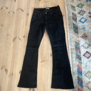 Svarta bootcut jeans med låg/mid midja - Svarta jeans från gina med bootcut-ben och låg/mid midja. Klassisk femficksmodell med kopparfärgade nitar och dragkedja. Jeansen är i stretchigt denimtyg och har raka bakfickor. Perfekta för en cool och avslappnad look.