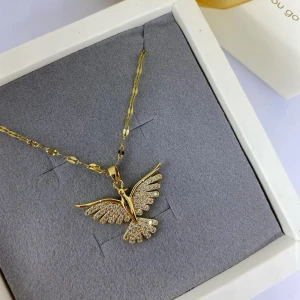 Guldigt halsband med fågelberlock - Snyggt halsband i guld med en fågelberlock som är täckt av glittrande stenar. Kedjan har ett unikt mönster och berlocken är detaljerad med utsträckta vingar. Ej använd utan kommer från min small business.