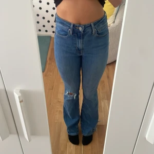 Levi's 725 High Rise Bootcut jeans - Säljer ett par Levi's Premium 725 High Rise Bootcut jeans i klassisk blå denim. De har hög midja, bootcut-ben och en snygg slitning på ena knät. Jeansen har fem fickor och Levi's ikoniska läderpatch bak. Perfekta för dig som gillar en tidlös och cool look.