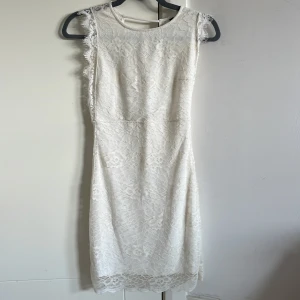 Vit spetsklänning med v-ringad rygg - Säljer en superfin vit kortklänning i spets med blommigt mönster. Klänningen är ärmlös och har en snygg v-ringning i ryggen. Perfekt för sommarens alla tillfällen! Materialet känns lätt och luftigt.