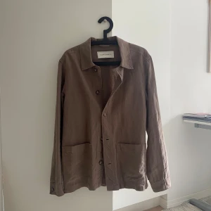 Grön overshirt från A Day's March - Säljer en grön overshirt från A Day's March i storlek small. Jackan är tillverkad i linne, har klassisk krage, knäppning framtill och två stora fickor. Perfekt för lager-på-lager och har en avslappnad vibe med lång ärm och enkel design. Ny pris 3500. Endast andvänd 2 gånger. Du kan även köpa till linnebyxorna i samma färg och isåfall skriv!