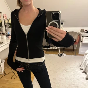 Tajt ziptröja från weekday  - Säljer en svart hoodie med dragkedja och huva. Tröjan har långärmade, ribbade muddar och en slim passform som sitter snyggt. Perfekt för dig som gillar en enkel och stilren look. Passar till jeans eller leggings och är superbekväm.