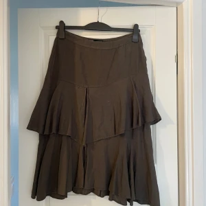 Brun volangkjol från Zara i linne - Supersnygg brun långkjol från Zara i linne med flera lager volanger. Kjolen har en avslappnad passform och är perfekt för dig som gillar en bohemisk och flowy stil. Dragkedja i sidan för enkel påklädning.