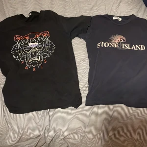 En kenzo och en stone Island T-shirt  - Svart t-shirt från Kenzo med ikoniskt tigertryck i flera färger och texten 'Paris' framtill. Klassisk passform och rund halsringning, perfekt för dig som vill sticka ut med en statement-piece.