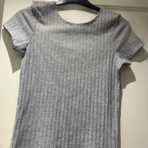Grå ribbad kortärmad topp - Säljer en enkel och stilren grå ribbad topp med korta ärmar och rund halsringning. Toppen har en rak passform och är tillverkad i ett mjukt material som känns skönt mot huden. Perfekt att matcha med jeans eller kjol för en clean look.