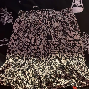 Svartvit leopardmönstrad kjol C M - Svartvit kortkjol från C i storlek M med leopardmönster och volang nertill. Kjolen har smock i midjan för en bekväm passform och är tillverkad i ett lätt och luftigt material. Perfekt för dig som gillar djurmönster och vill sticka ut.