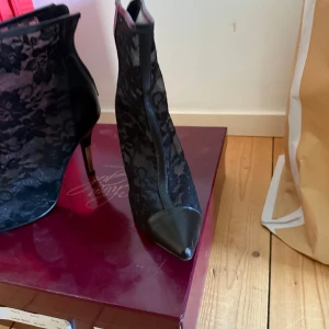 Svarta spetsiga stövletter med spets - Säljer ett par svarta stövletter från China Girl med spetsig tå och hög klack. Skorna är täckta av ett blommigt spetsmönster och har detaljer i skinnimitation framtill och längs sidorna. Perfekta för dig som vill sticka ut med en elegant och edgy look.