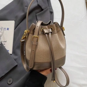 Beige bucket bag med snörning - Trendig beige bucket bag med snygga gulddetaljer och justerbar axelrem. Väskan har en cool snörning upptill och är tillverkad i en mix av syntetmaterial och skinnimitation. Perfekt storlek för det viktigaste och ger en stilren touch till din outfit.