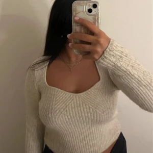 Beige stickad tröja med v-ringning - Superfin beige stickad tröja med djup v-ringning och lång ärm. Tröjan har en ribbad struktur och sitter tajt men bekvämt. 