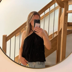 Svart halterneck linnetopp - Säljer en svart halterneck linnetopp med lös passform och ärmlös design. Toppen har en enkel och stilren look med tunna band som knyts i nacken. Perfekt att matcha med jeans eller kjol för en trendig vibe.