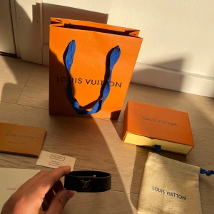 Svart armband i skinn - Exklusivt svart armband med metall framtill. Tillverkat i äkta skinn med stilren design och silverfärgad detalj. Kommer med originalförpackning, dustbag och certifikat. Perfekt accessoar för dig som gillar lyx och streetstyle.