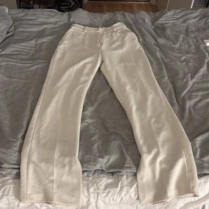Beige kostymbyxor från NA-KD - Snygga beige kostymbyxor från NA-KD i storlek 36. Byxorna har raka ben, hög midja och klassiska fickor bak. Materialet är mjukt och har en lätt glansig finish som ger en fräsch och stilren look. Perfekta för att dressa upp din outfit.