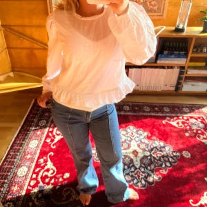 Vit blus med volang och puffärm - Säljer en söt vit blus med volangkant och puffiga långärmar. Blusen har en rund halsringning med liten volang och är tillverkad i ett lätt, krispigt bomullstyg. Passformen är normal och blusen har en feminin, romantisk vibe som är enkel att styla.