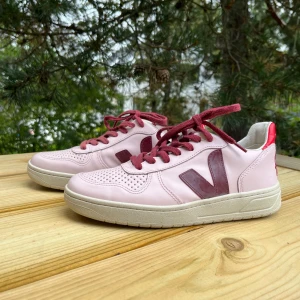 Rosa Veja sneakers - Säljer ett par unika ljusrosa Veja sneakers med vinröda snören och V-logga. Ett av snörena är lite blekare i färgen än det andra, men är inget som förstör looken! Baksidan har röda detaljer och den broderade texten ”first lady”. Älskar färgkombinationen av rosa och det röda! Hör av dig om du har mer frågor:)